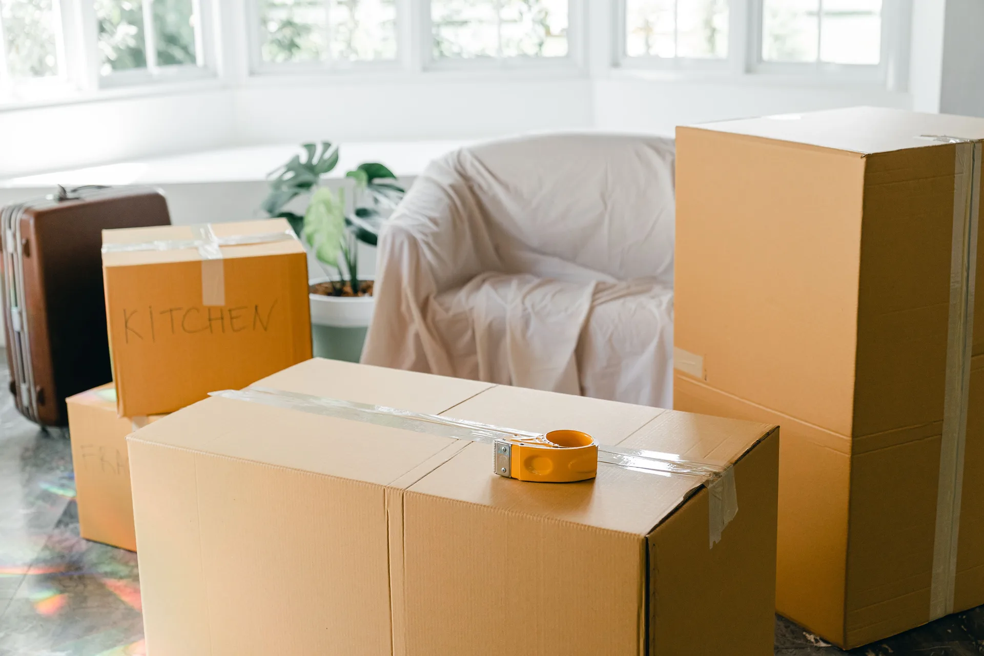 Cardboard moving boxes labelled by room in a bright empty living room before a move