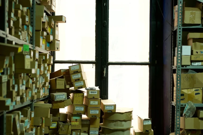 Cardboard boxes and household belongings stacked in a room by a window