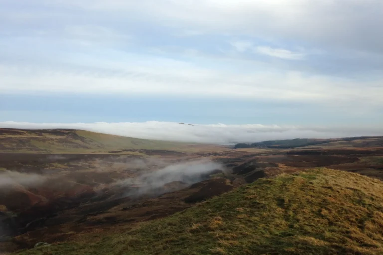 Rolling hills of the Scottish Highlands under low mist and blue sky
